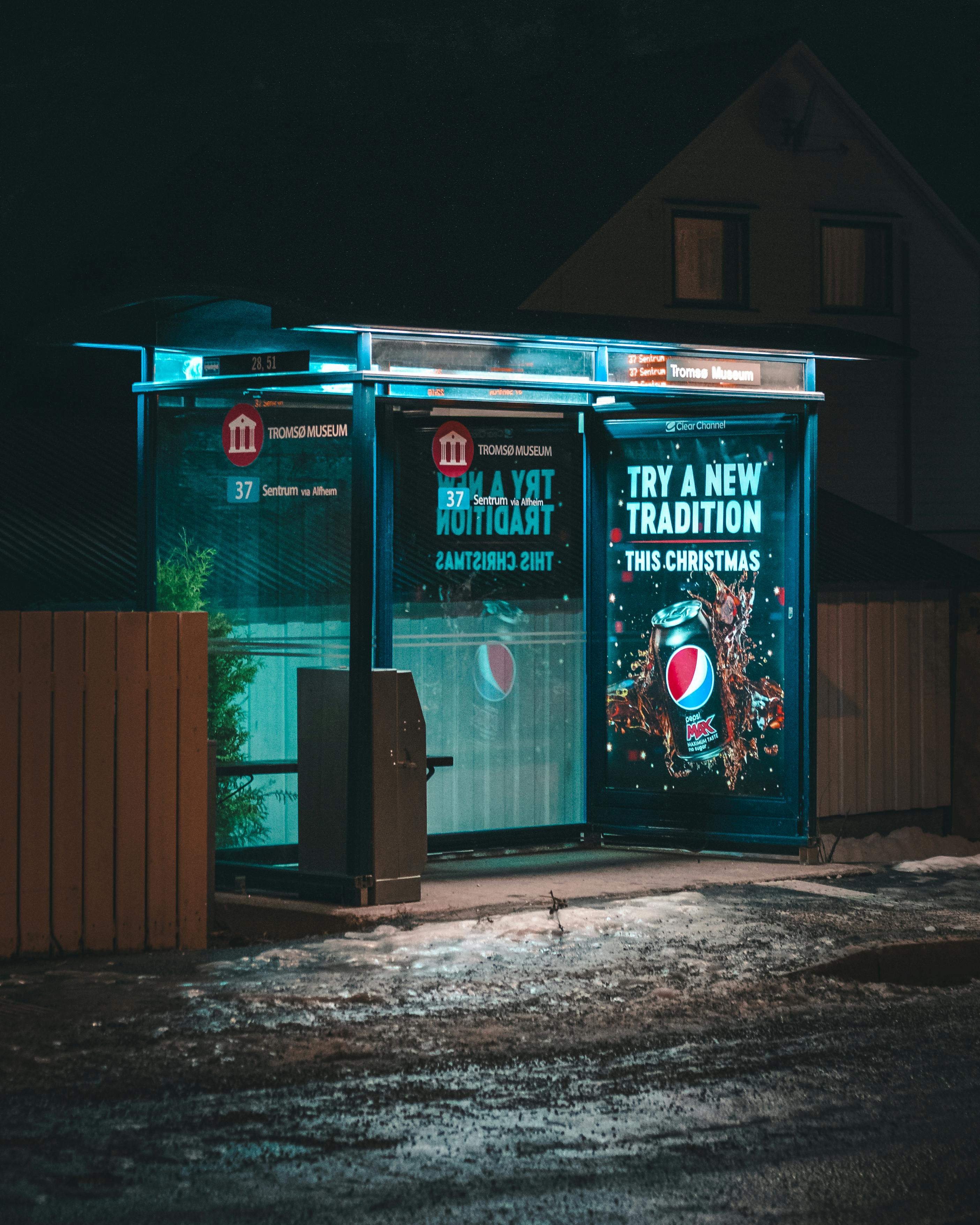 An empty bus stop with glowing advertisements at night, reflecting on wet pavement.