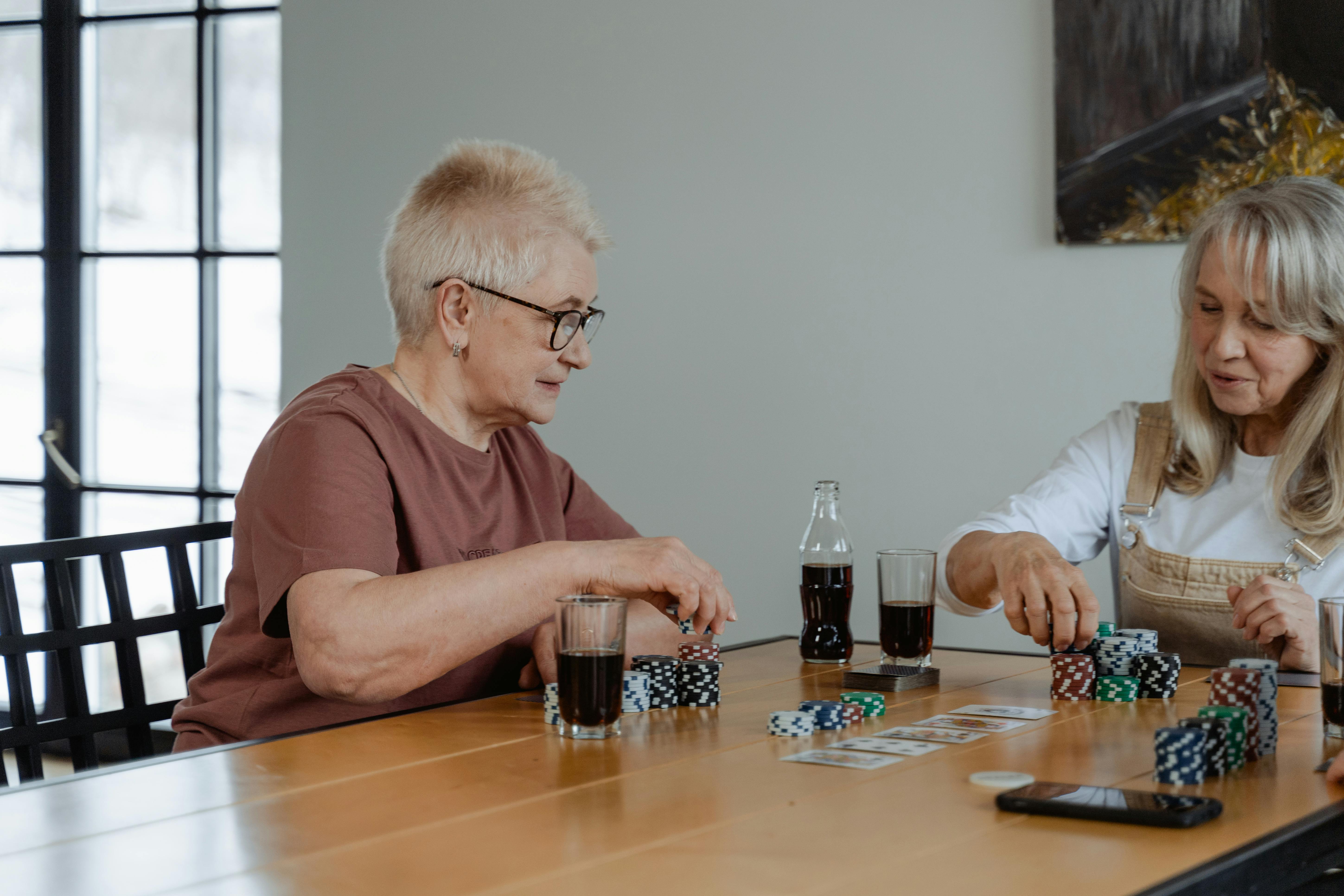 Two senior women enjoying a game of poker at a table indoors, surrounded by poker chips and cards.
